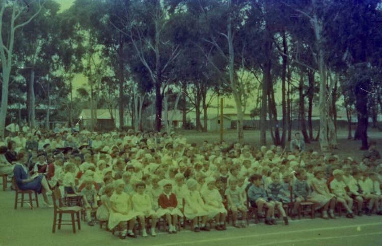 A photo of school assembly in the outdoor playground surrounded by trees.